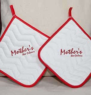 white pot holder in red boarder with Mothers New Orleans print at the center